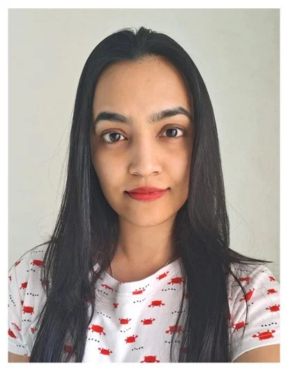 A young woman with long black hair and light brown skin, wearing a white shirt with red fish print, stands against a plain light-colored wall.
