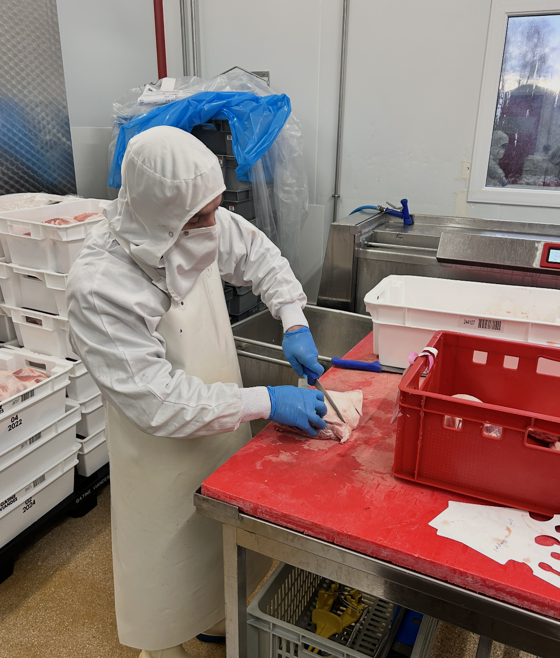 Charcutier qui coupe de la viande de porc dans l'atelier Pierrat