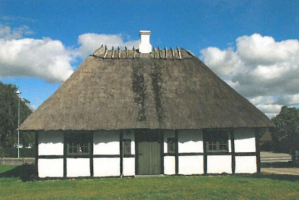 Traditionelt bygget hus med stråtag og hvid væg med sorte bindender