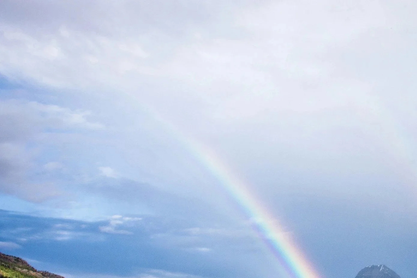 En regnbåge som sträcker sig över en himmel med moln, med ett berg i bakgrunden.