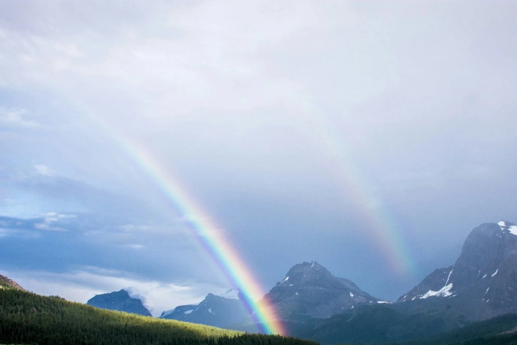 Regnbåge över bergslandskap med molnigt himmel
