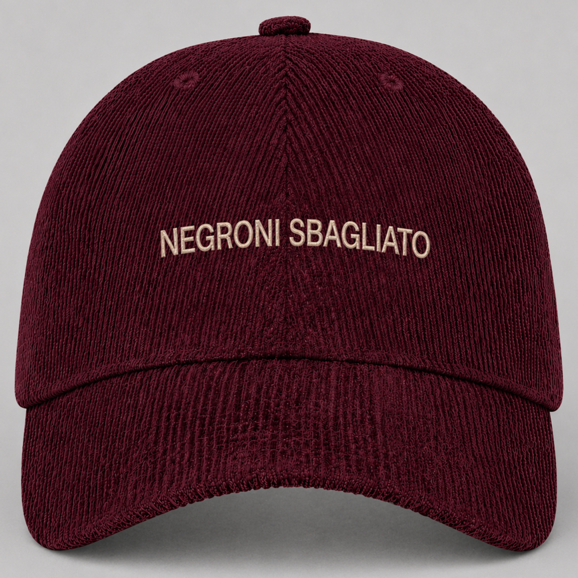 Casquette rouge foncé en tissu côtelé avec le texte "NEGRONI SBAGLIATO" brodé en blanc sur le devant.