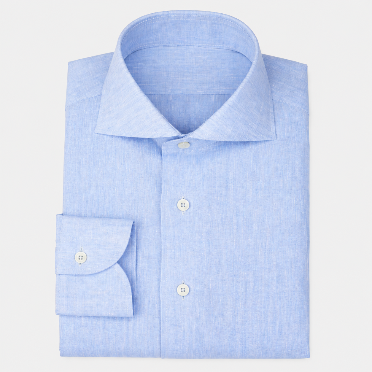 Chemise bleue en lin avec col classique, boutons blancs et poignets boutonnés, pliée sur un fond blanc.