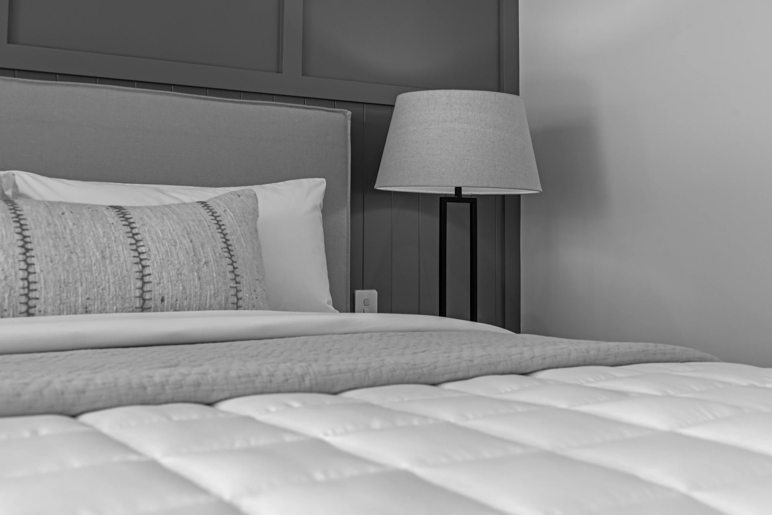 Close-up of a bed with pillows and a bedside lamp in a bedroom.