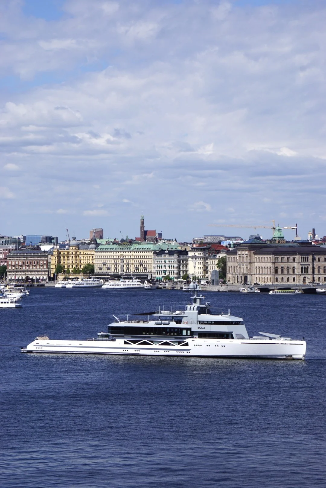 View of a city skyline with historic buildings, a river, and a large white yacht sailing.