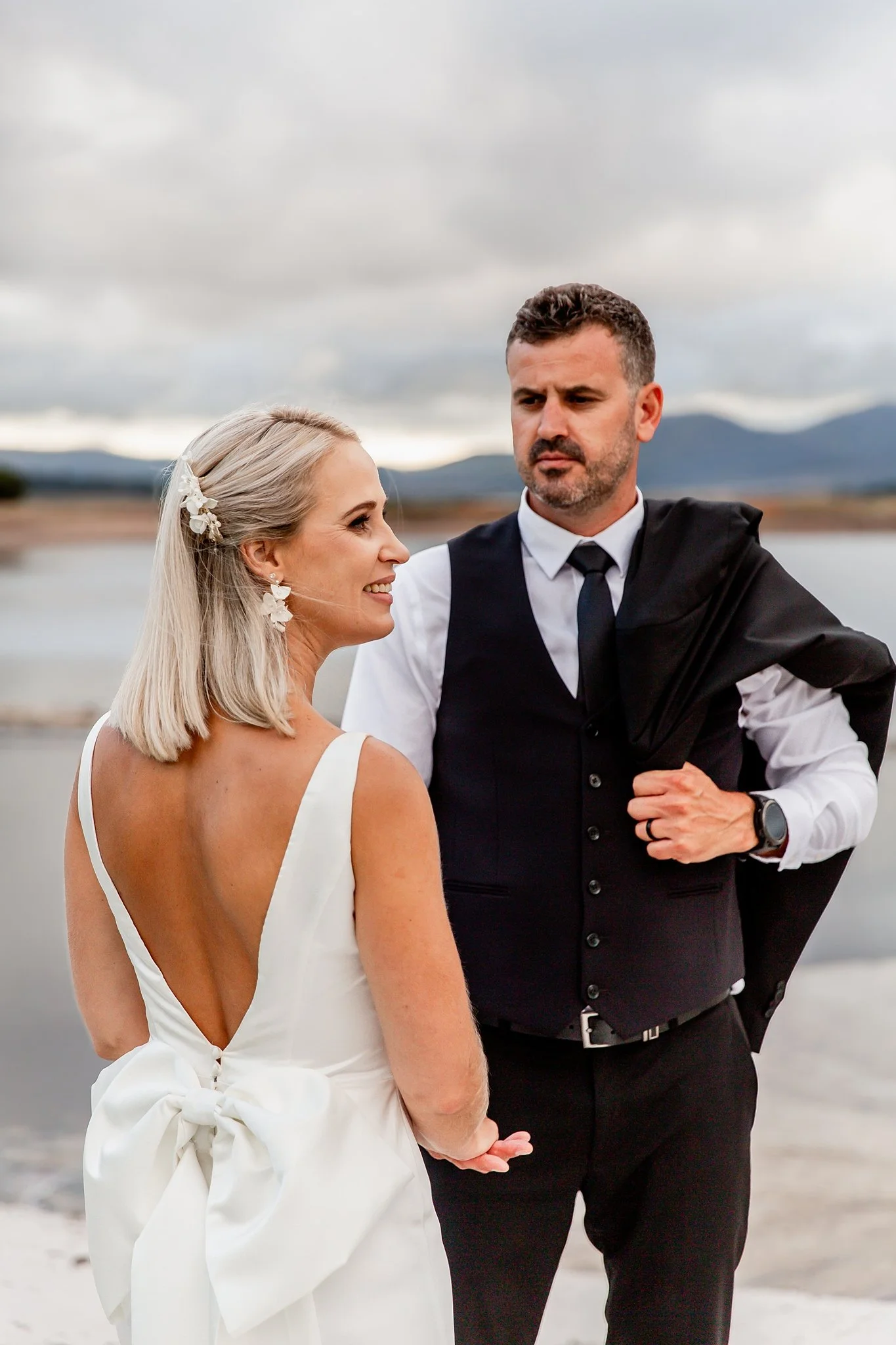 bride and groom holding hands. Groom looking at bride with blazer over his shoulder.