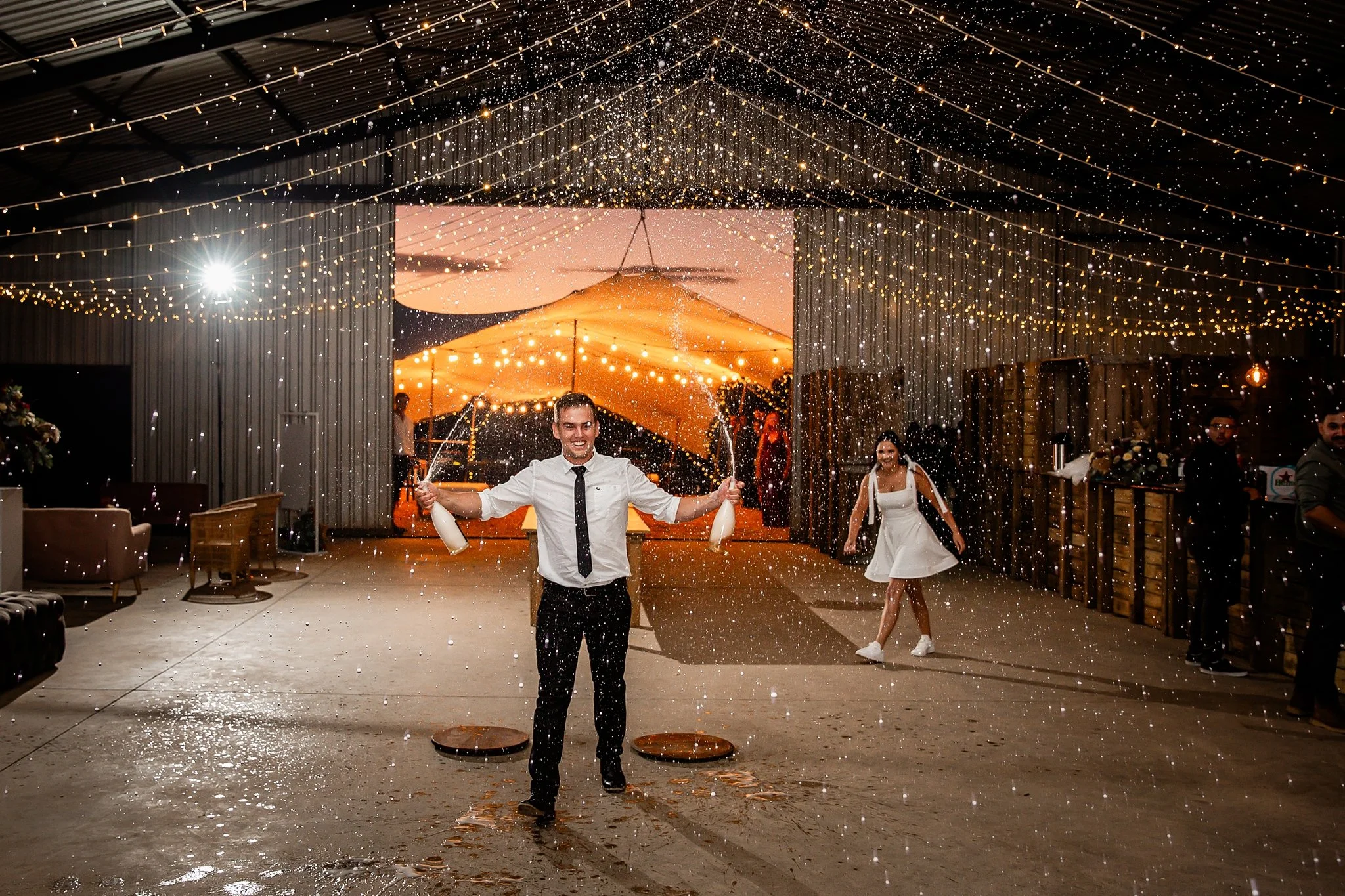 Man celebrating with party poppers in a decorated venue adorned with string lights at night.