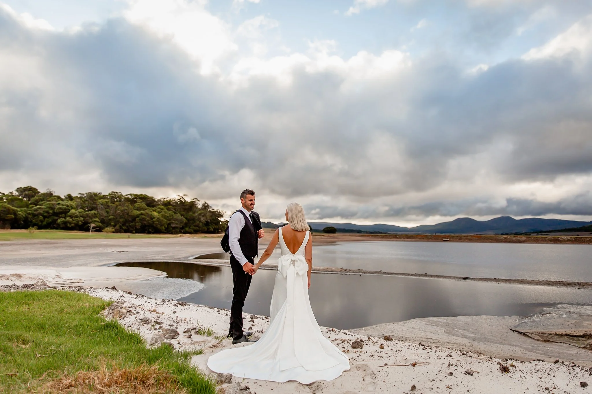 Wedding couple holding hands. Standing on white sand at a dam.