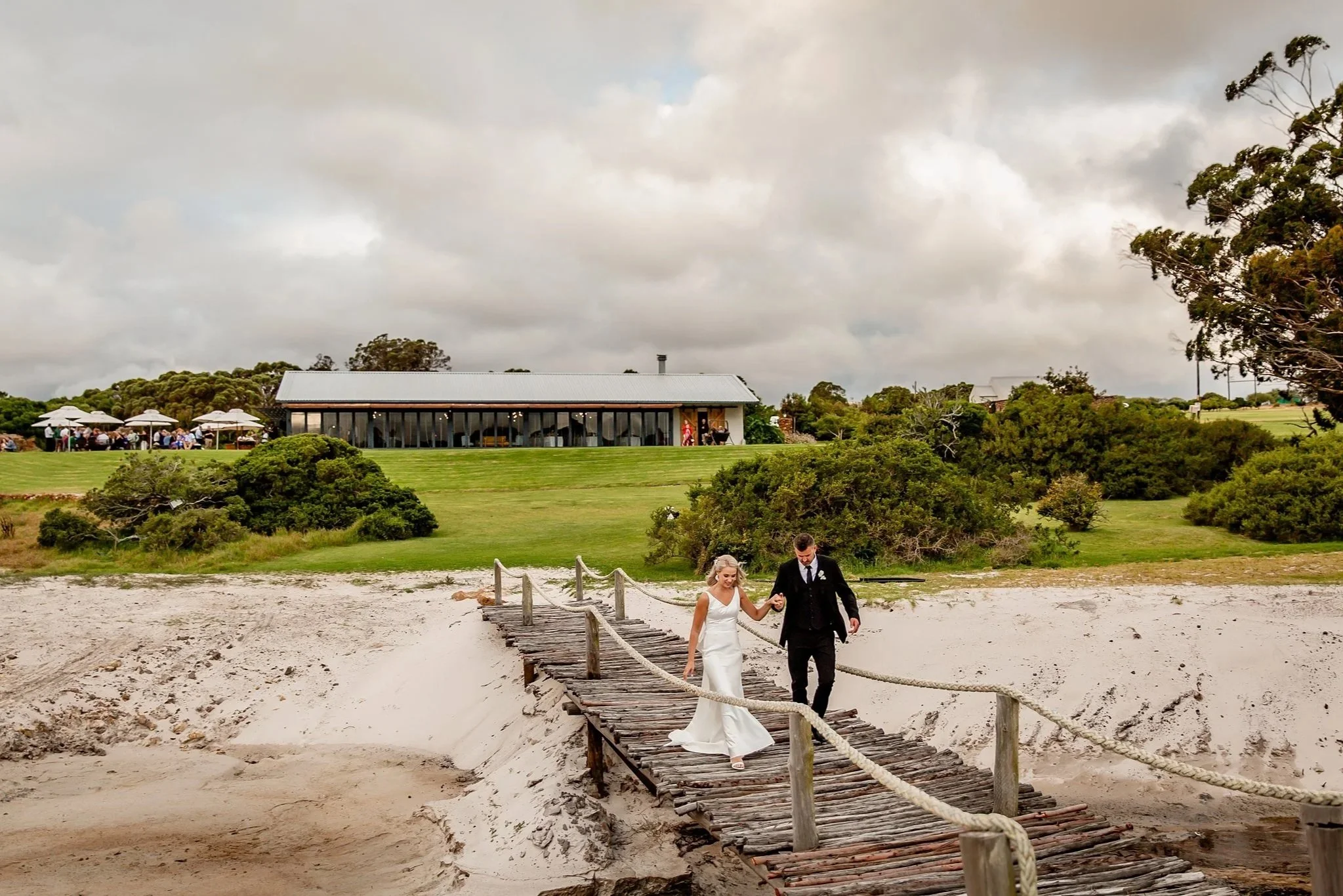 Wedding couple walking over a bridge with their venue in the background.