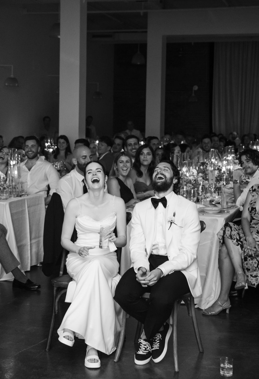 Groupe de personnes assises à une table lors d'un mariage ou d'une fête, riant et souriant, ambiance festive et joyeuse.