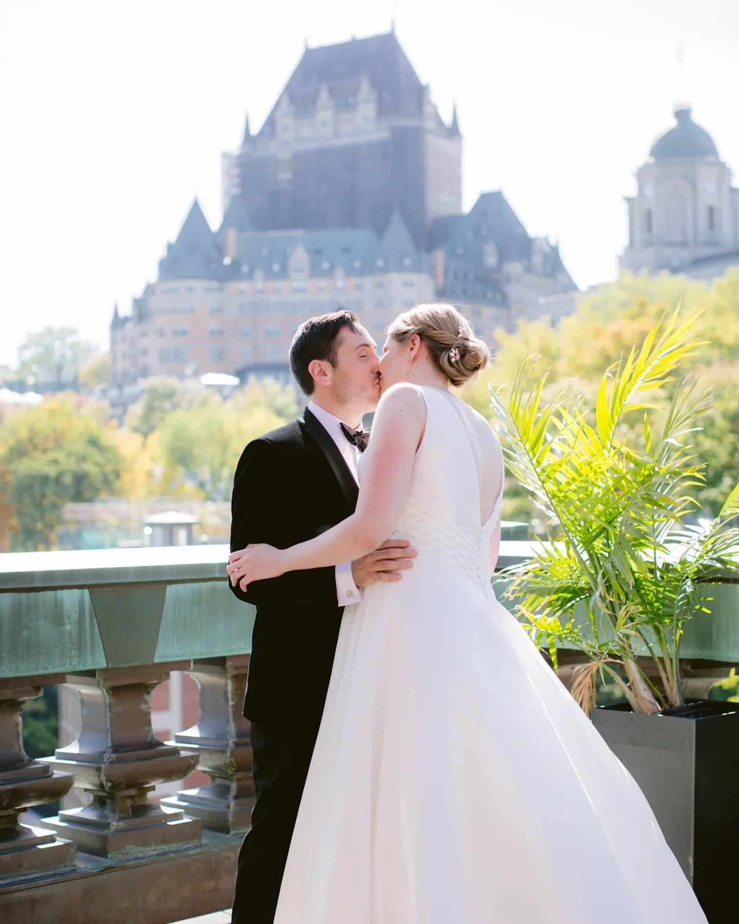 Un couple élégant s'embrasse sur un balcon avec le château Frontenac de Québec en arrière-plan, en plein air, lors d'un mariage.