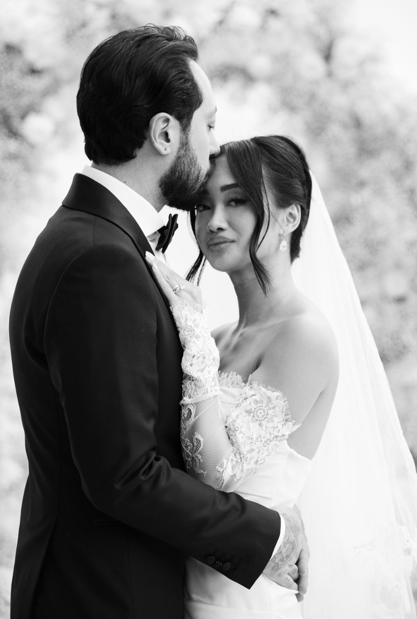 Un couple de mariés en costume et robe de mariage, en noir et blanc, partage un moment d'amour lors d'une séance photo.