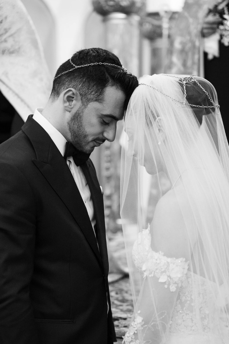 Un couple de mariés en prière ou méditation lors de leur mariage, la tête appuyée l'une contre l'autre, avec une robe de mariée élégante et un costume noir.