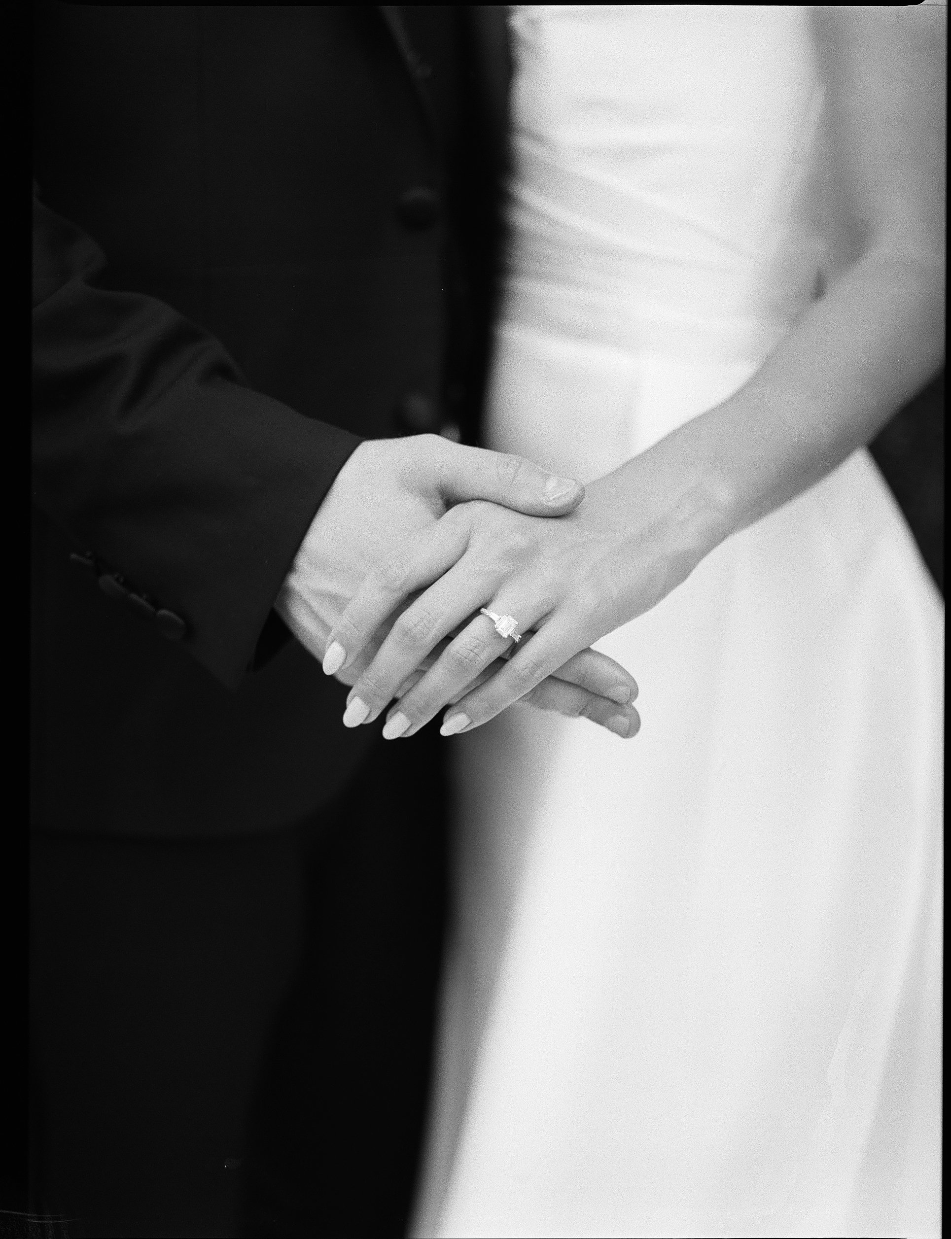 Married couple holding hands, close-up, focus on wedding ring, in black and white.