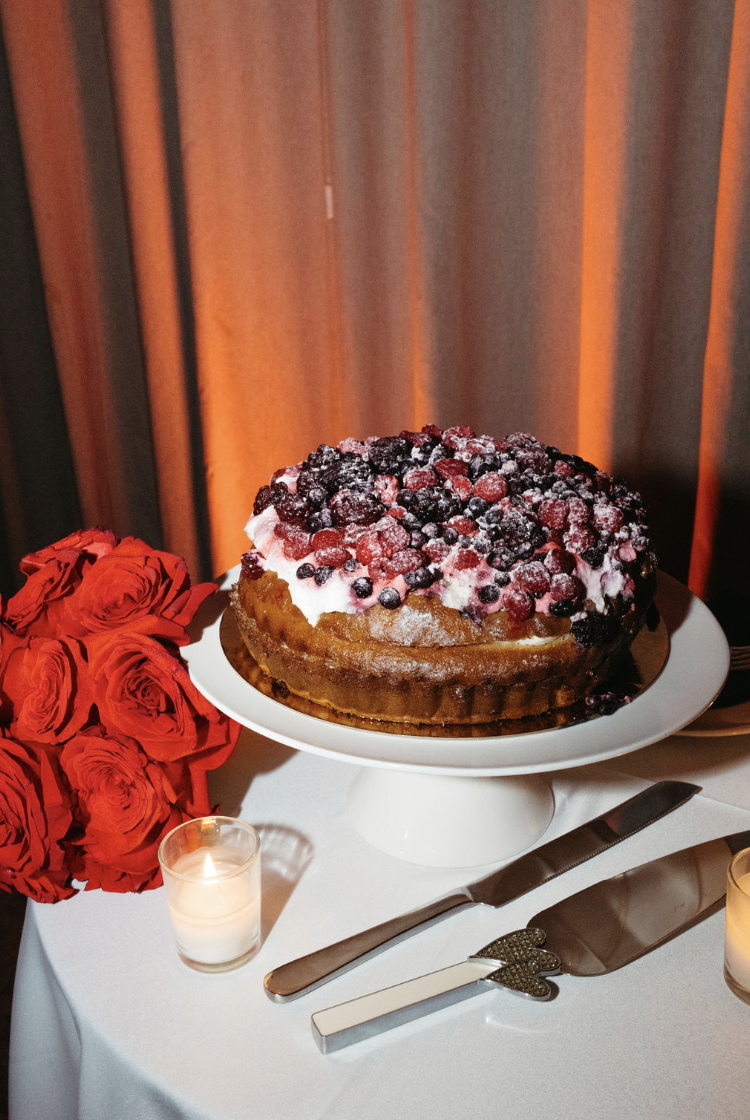 Gâteau de mariage aux fruits rouges et crème, décoré de fruits rouges congelés, présenté sur un plat, avec des roses rouges et des bougies à proximité sur une table