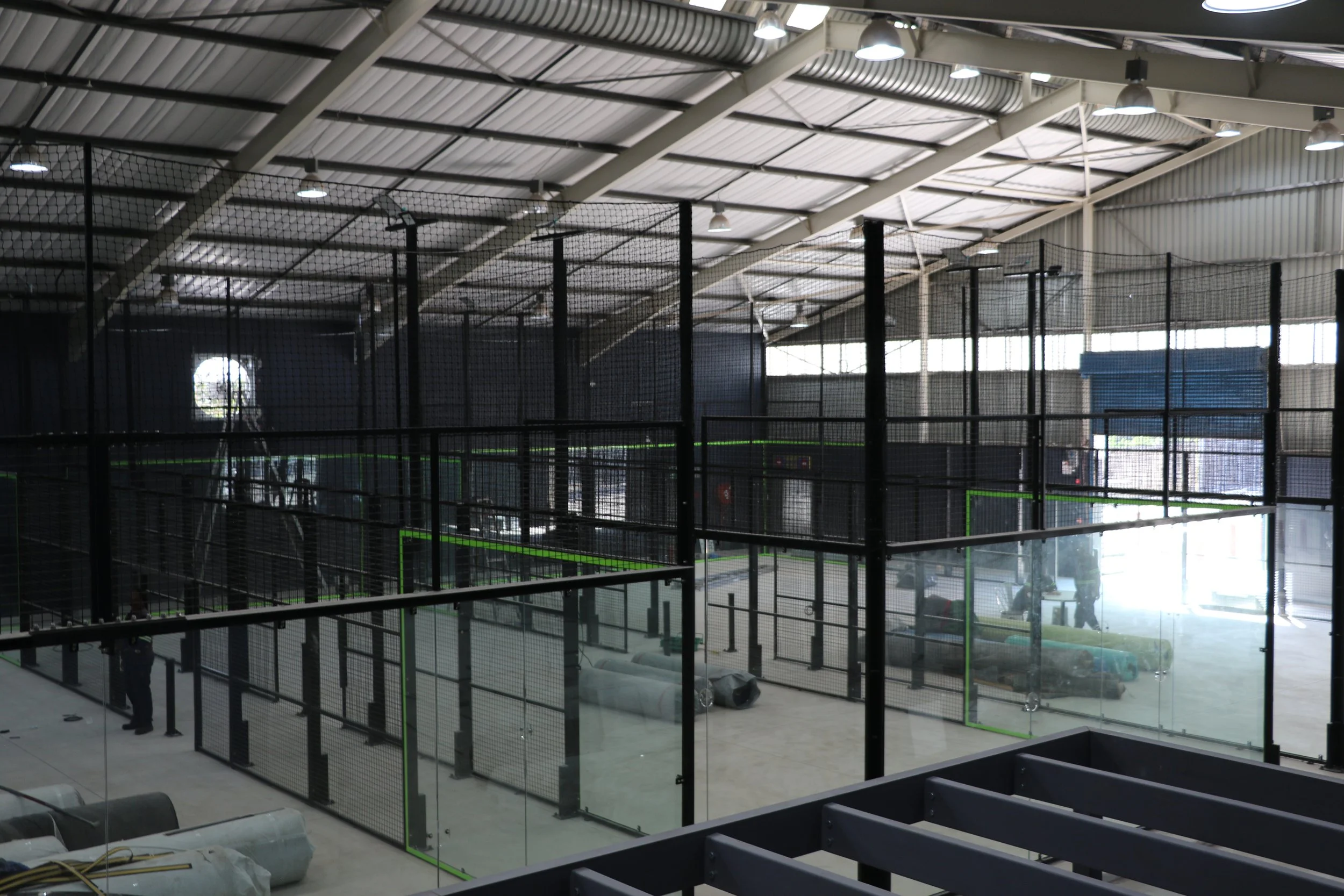Indoor padel facility under construction with multiple enclosed areas, scaffolding, and workers.