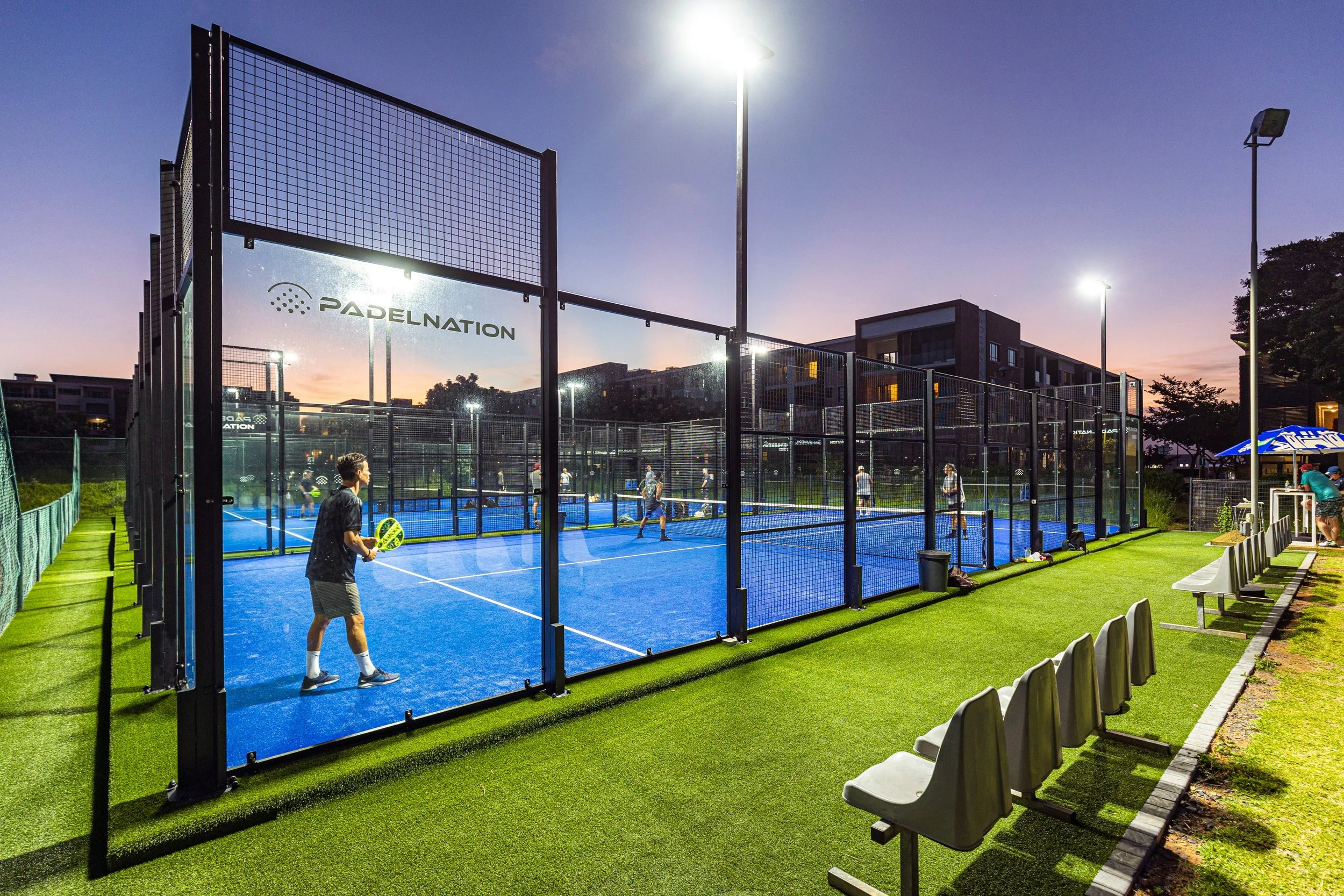 People playing padel during sunset with the lights on at PadelNation Umhlanga Country Club.