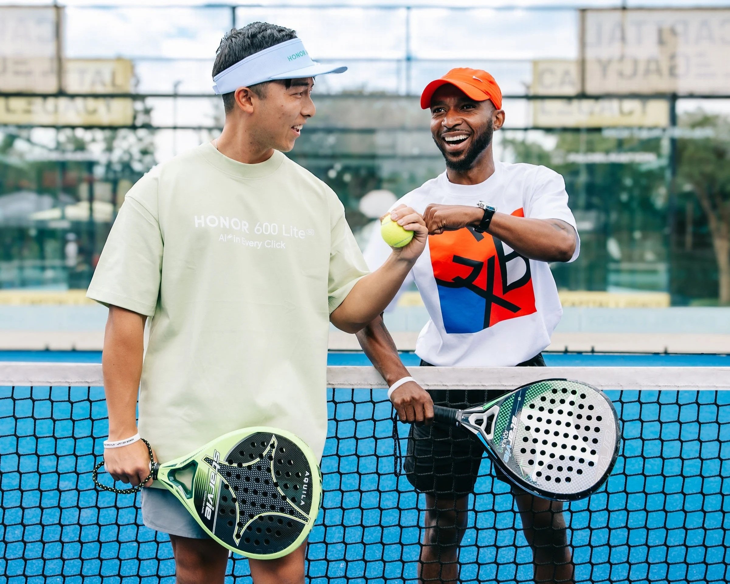 Two men holding pickleball paddles, smiling, standing behind a tennis net on a pickleball court.