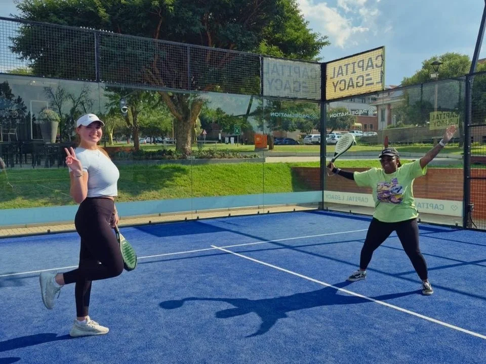 Two women playing pickleball on a blue court, smiling and posing for the camera.