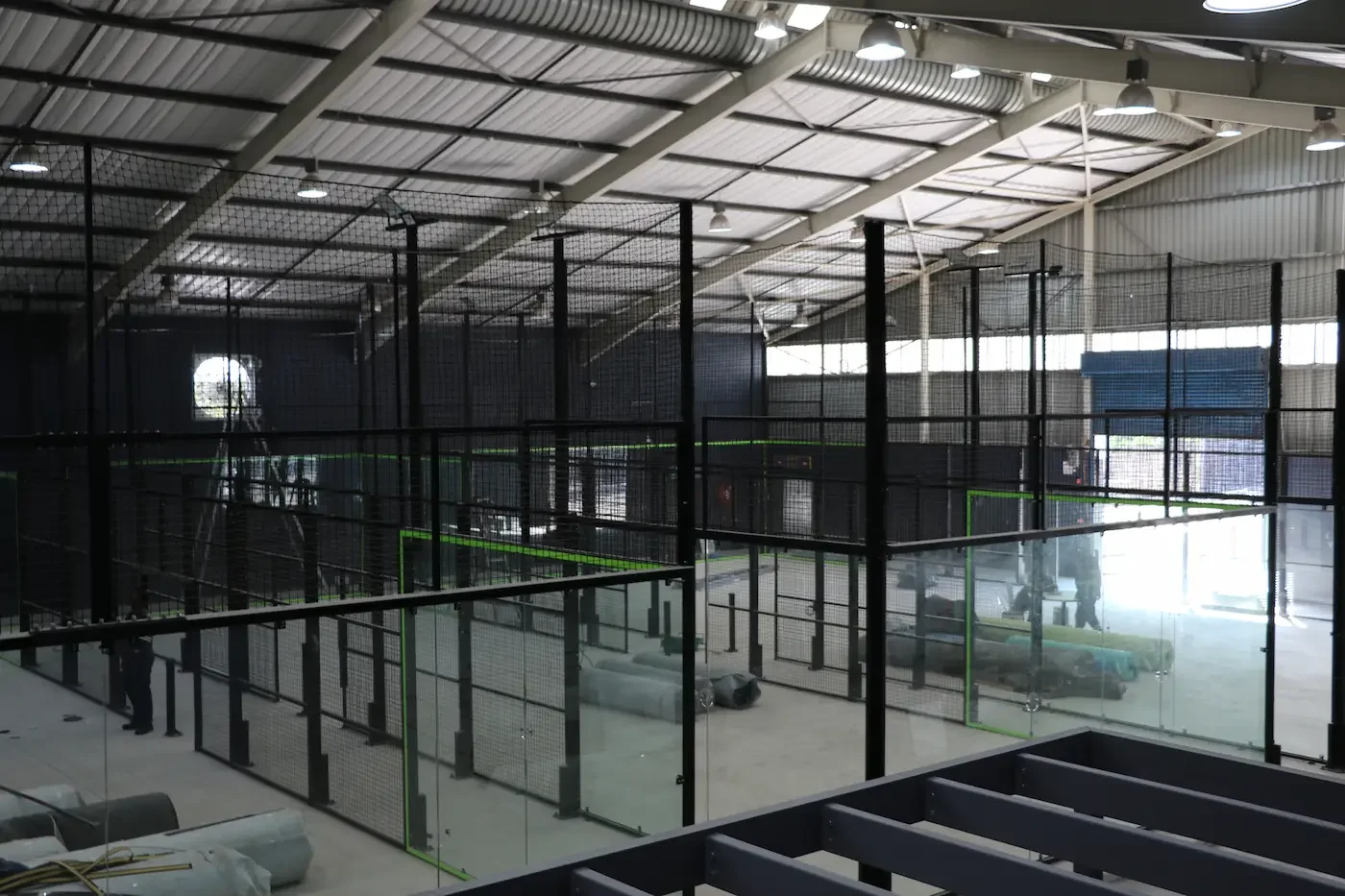 Indoor padel facility under construction with multiple enclosed areas, scaffolding, and workers.