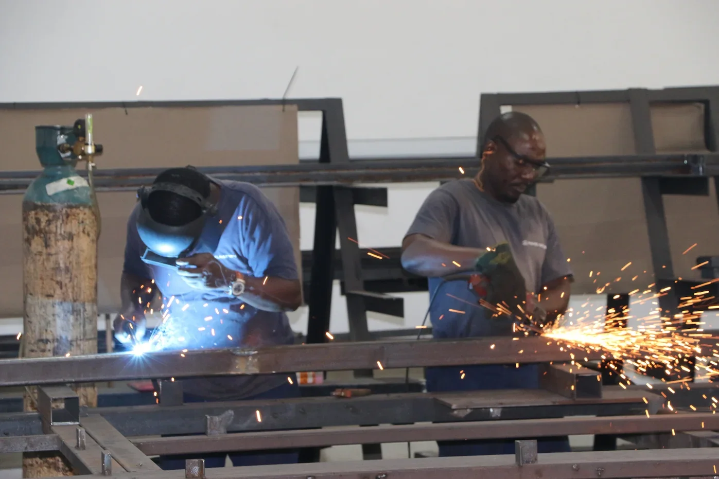 Two factory workers welding steel frames for a a padel court.
