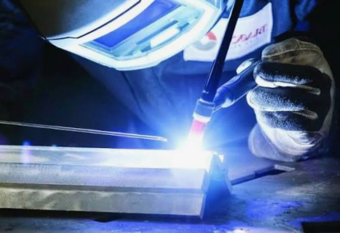 A person welding metal with a welding torch, sparks and bright light visible.
