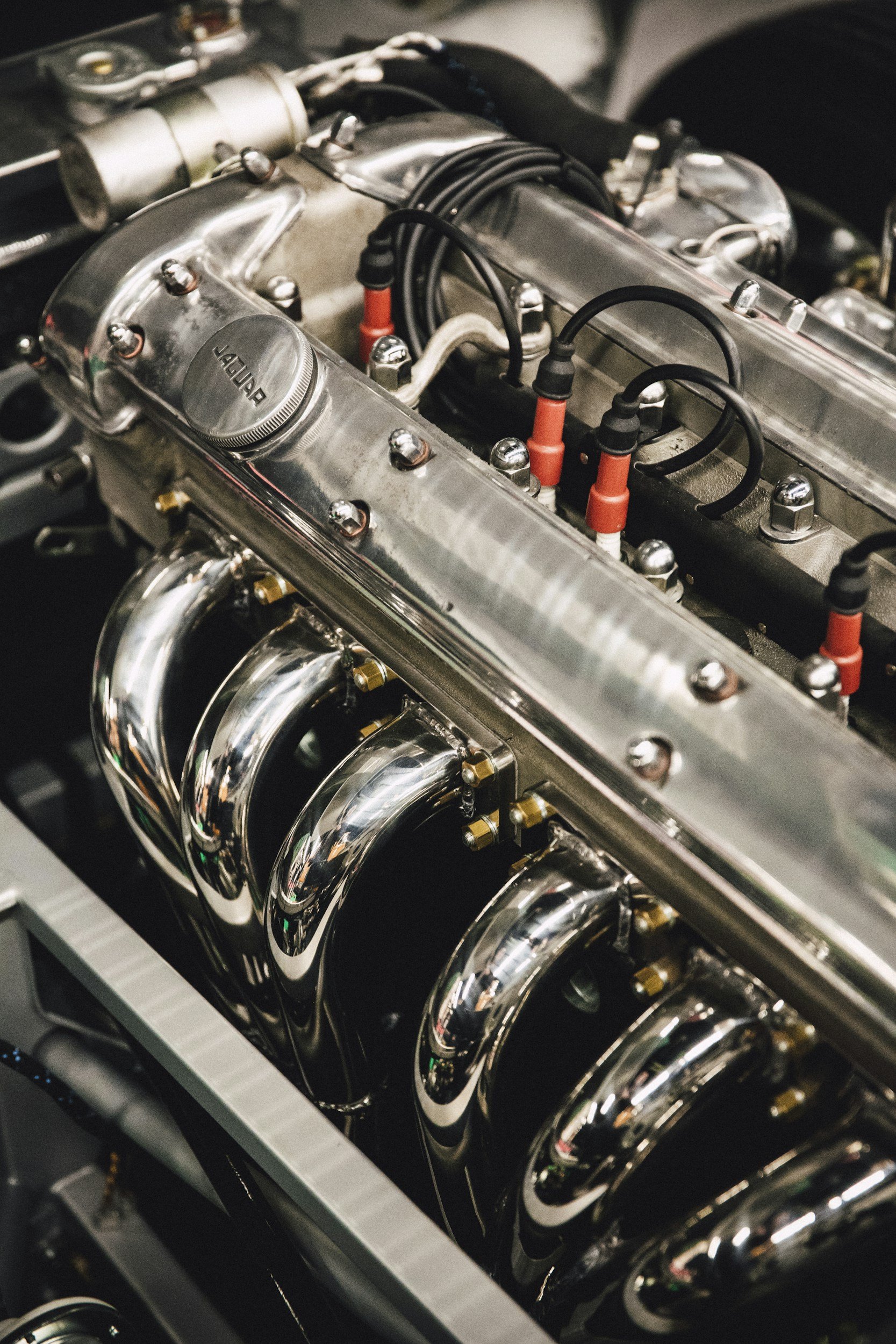 Close-up view of a vintage car engine with polished metal components, spark plug wires, and exhaust pipes visible.