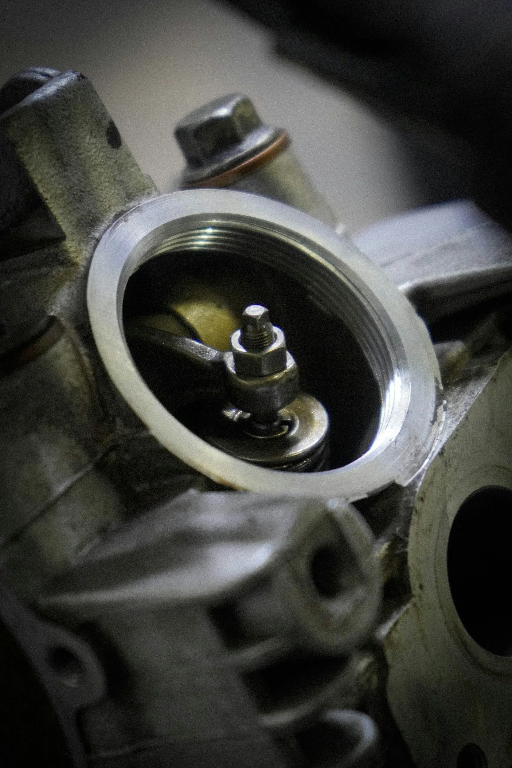 Close-up view of an engine component, showing a metallic circular opening with a spring inside, surrounded by engine parts and a bolt.
