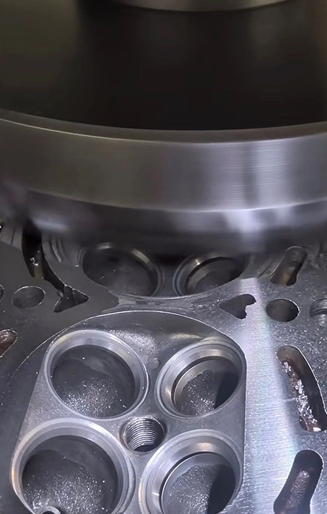 Close-up view of a metal engine cylinder head with multiple valve openings and a large piston in the background.