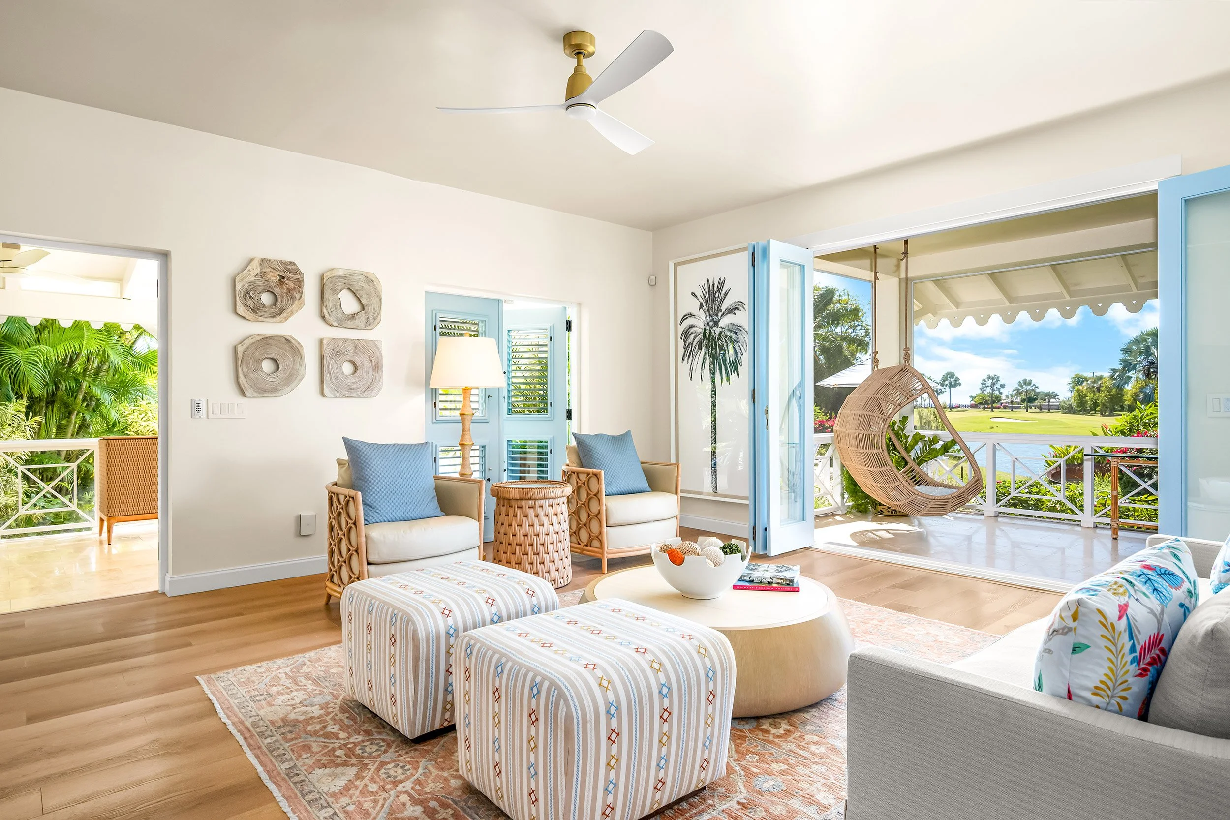 Living room with light-colored furniture, blue accents, potted plants, and a balcony view of a garden and lake.