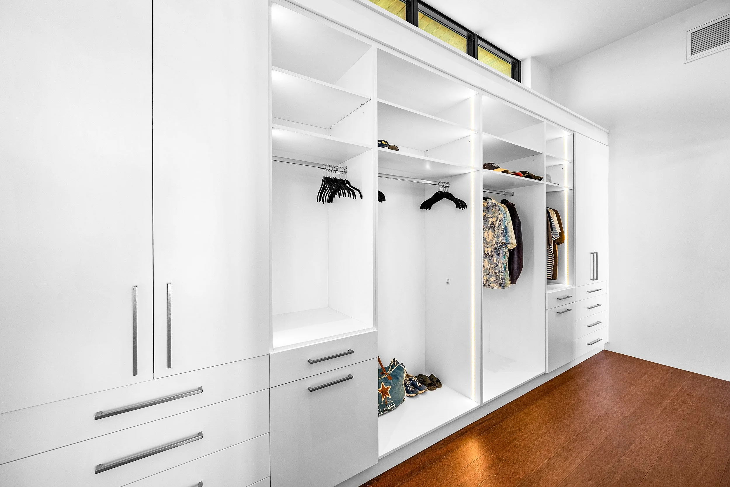 Modern white closet with open shelves and hanging space, displaying shoes and clothing, with a wooden floor.