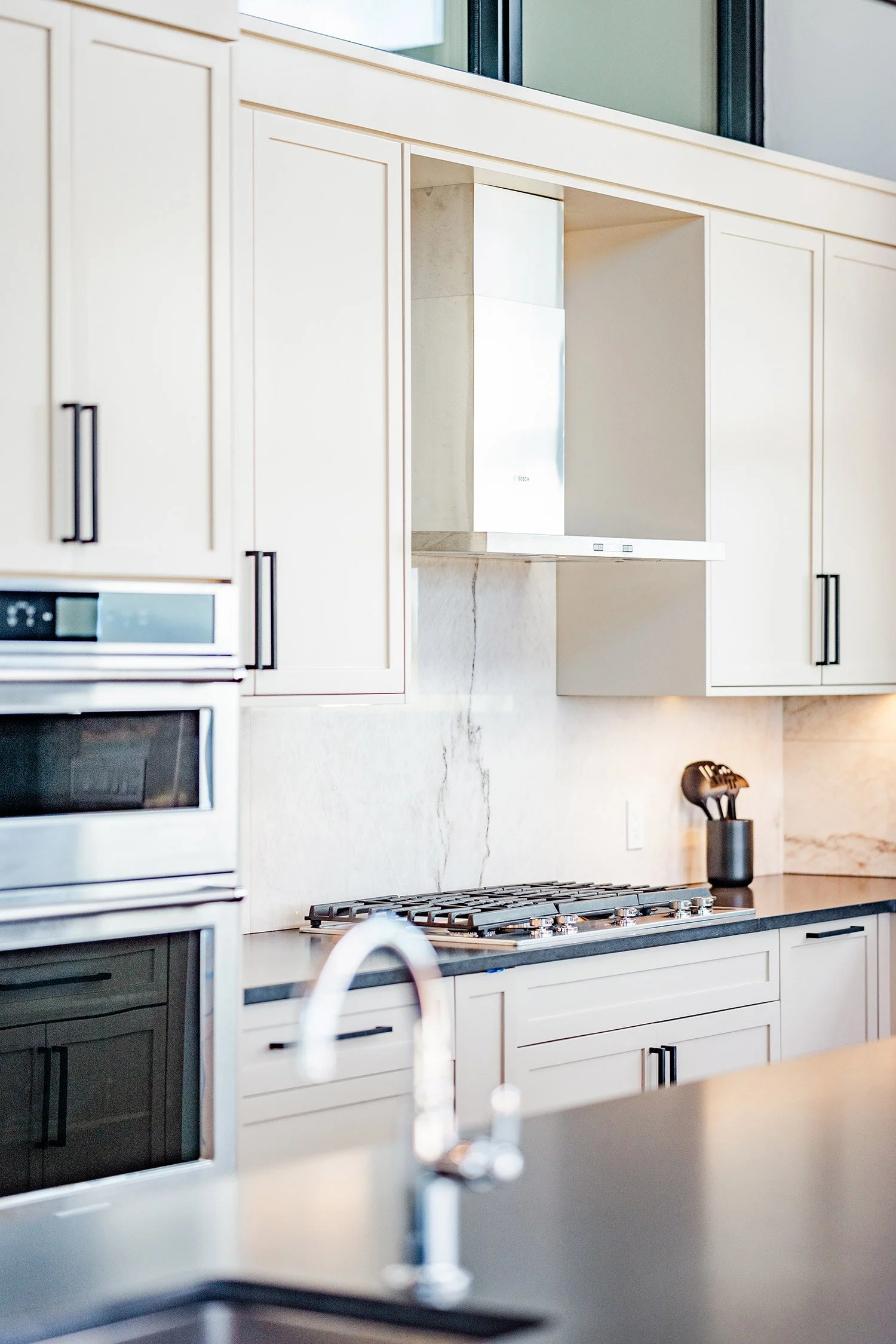 Modern kitchen with built-in oven, gas stove, white cabinetry, and a stainless steel range hood.