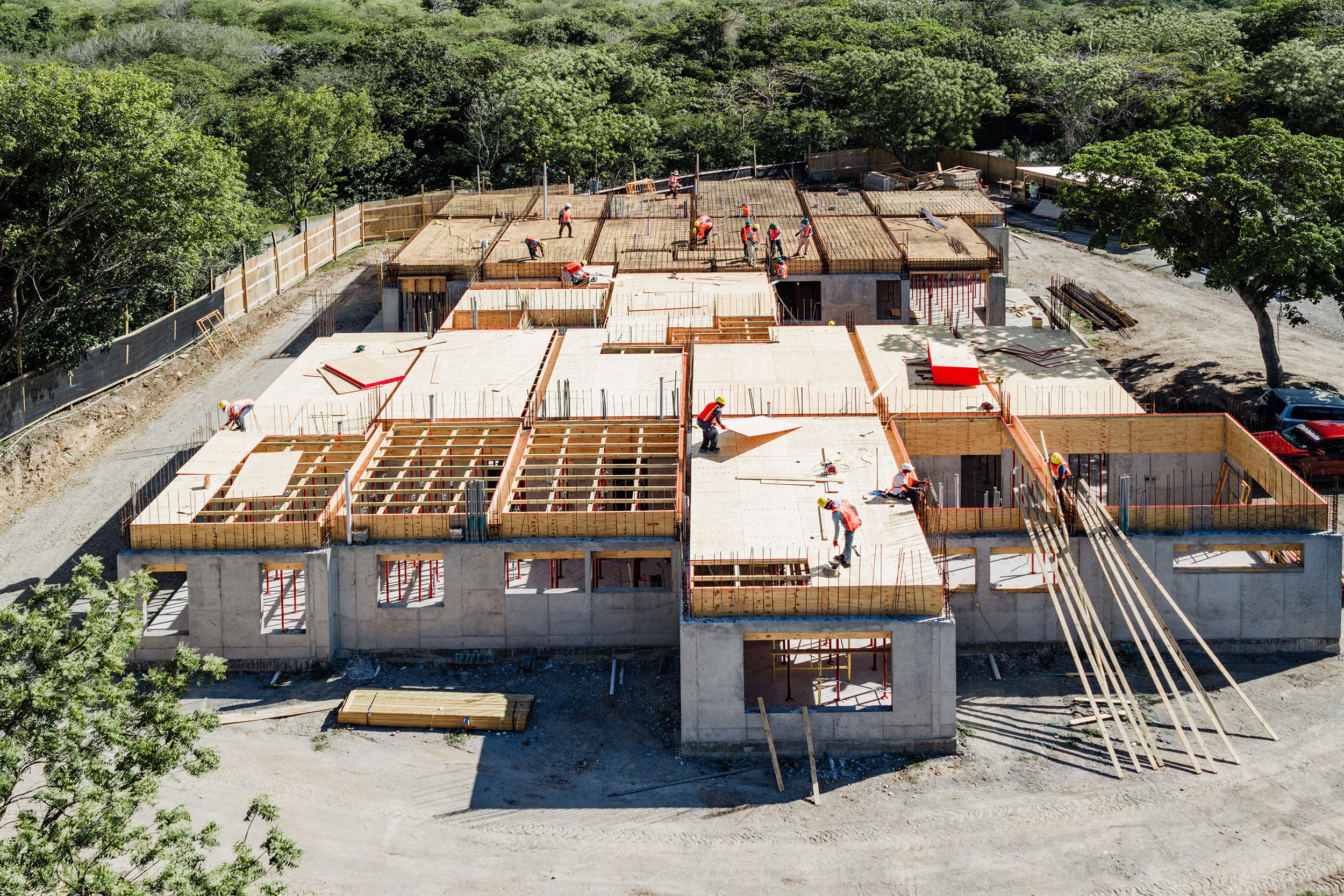 Aerial view of a construction site with workers pouring and smoothing concrete for building foundation in a forested area.