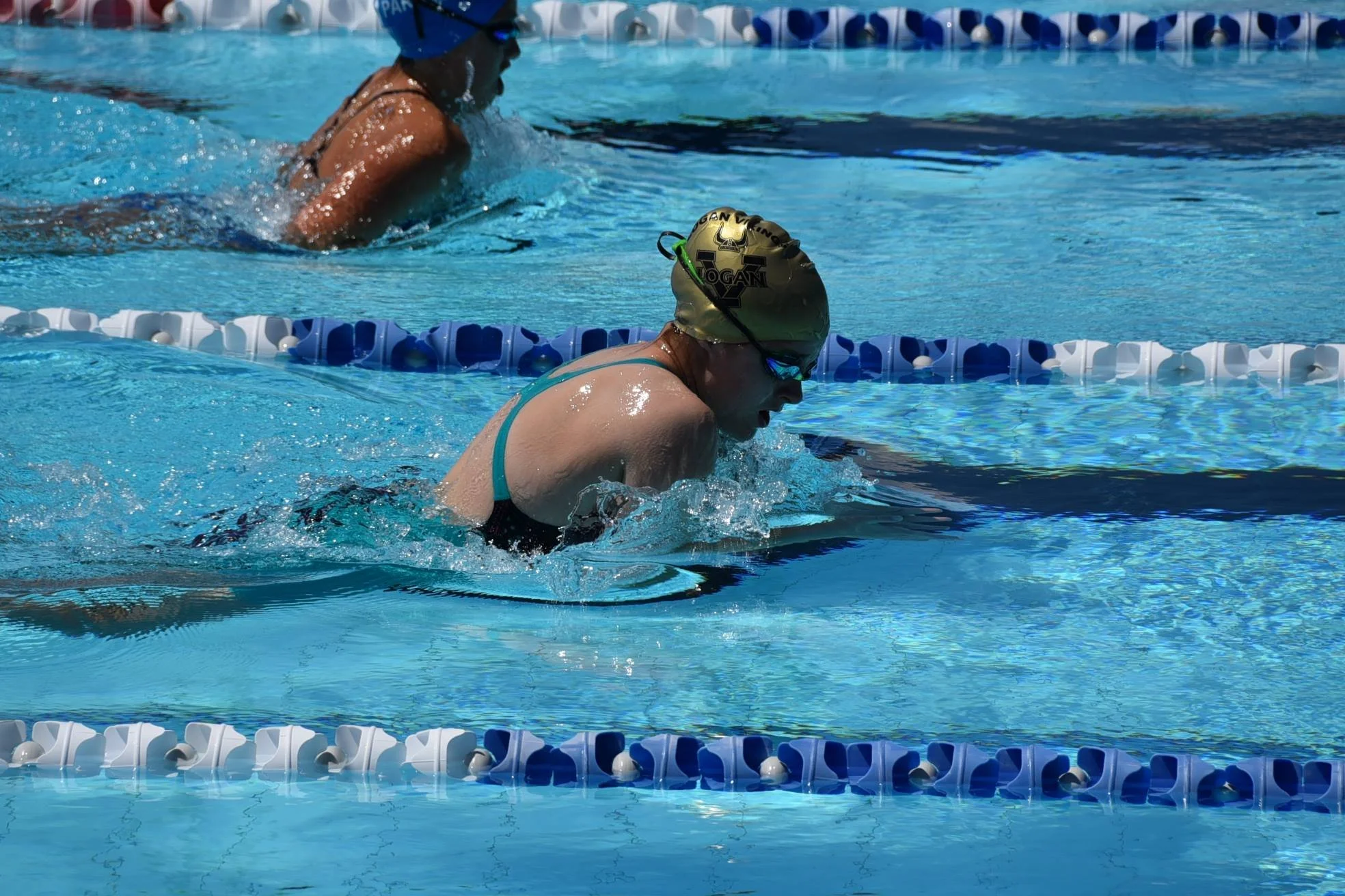 Swimmer in a turquoise swimsuit and gold swim cap swimming in a pool with blue and white lane dividers.