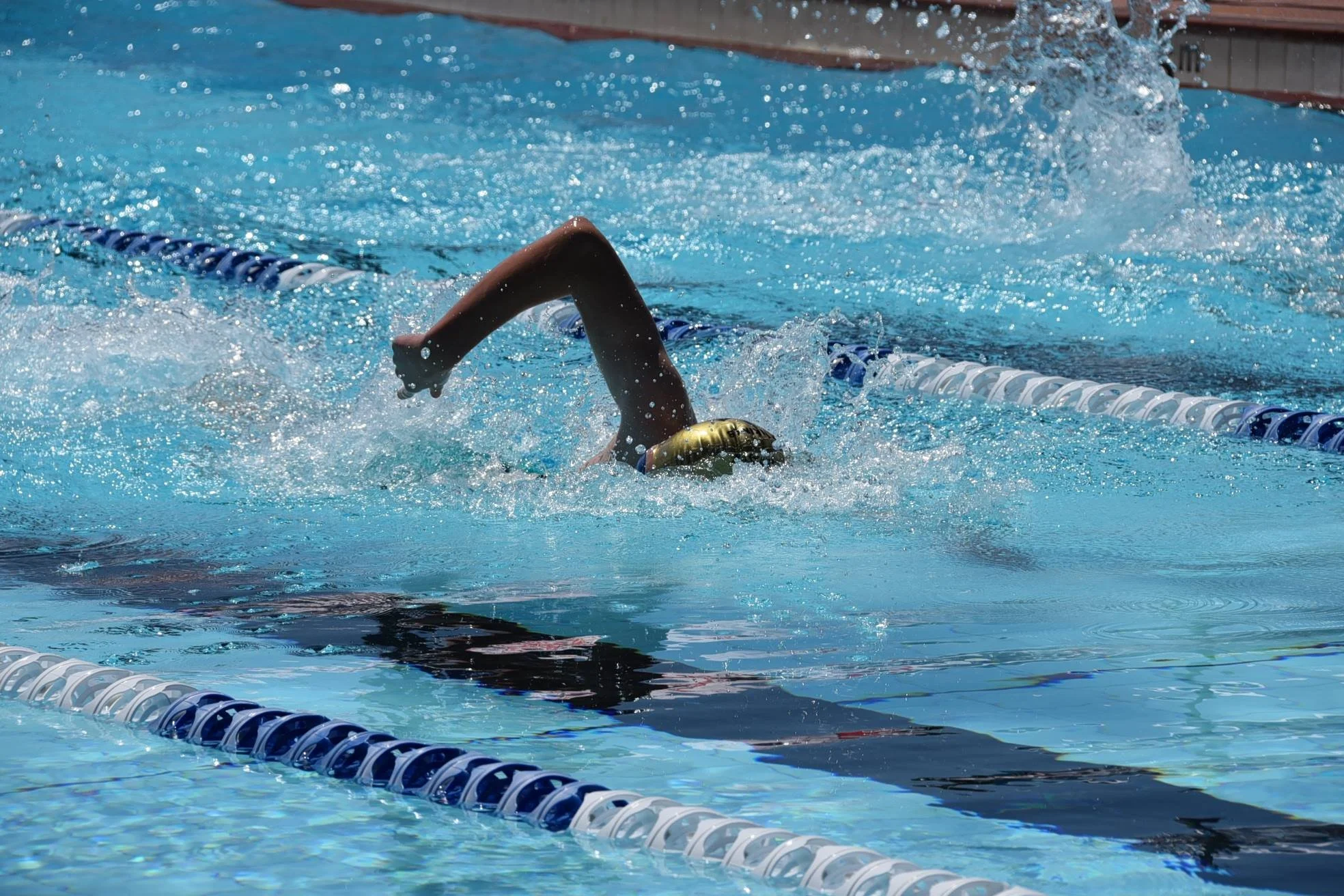 Swimmer in a swimming pool performing a freestyle stroke, wearing a swim cap and goggles.