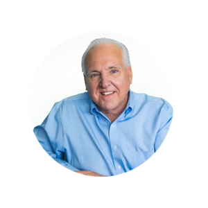 A smiling older man with white hair wearing a light blue shirt, posing against a white background.