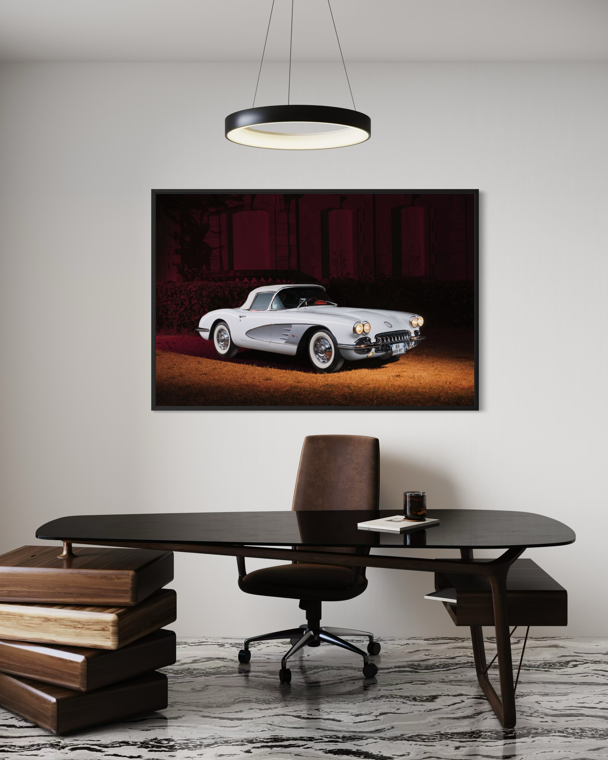 Une salle de réunion moderne avec un tableau sur le mur représentant une voiture ancienne blanche. Il y a un bureau en bois sombre, une chaise de bureau noire avec roulettes, un verre et un livre sur le bureau, et un lampadaire suspendu au plafond.