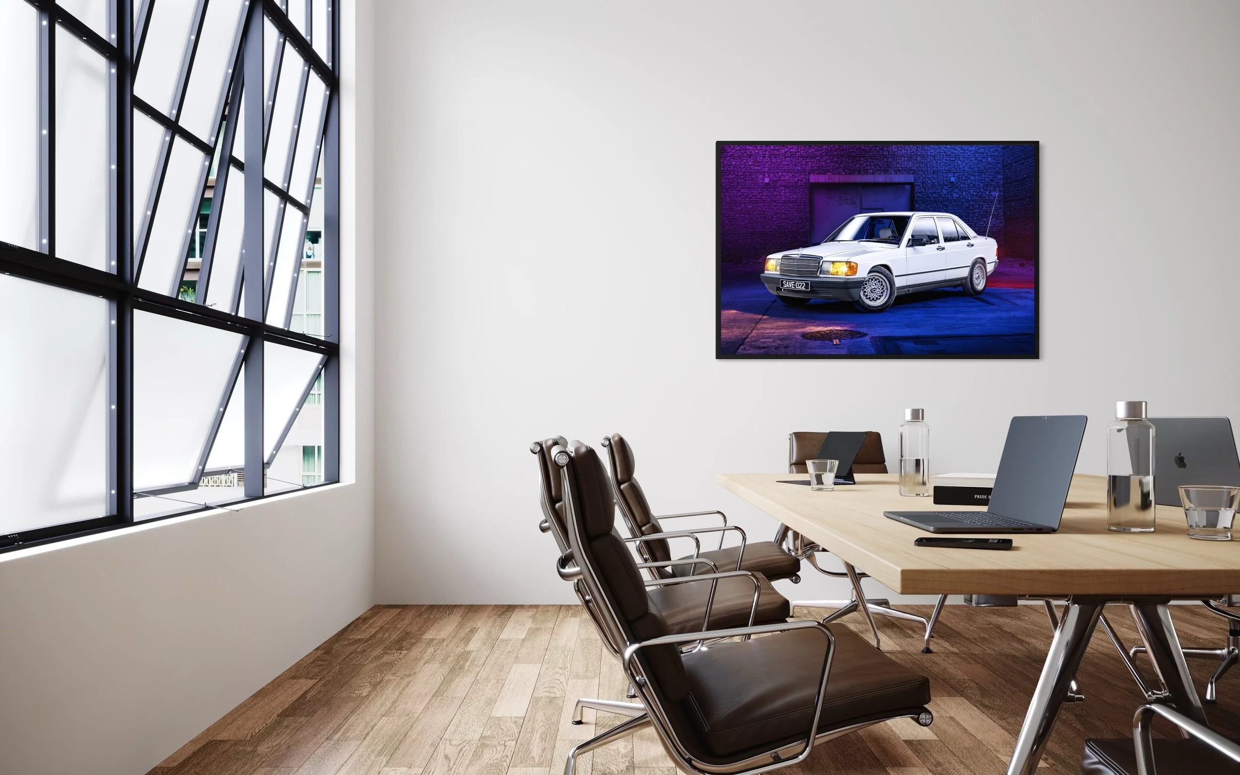 Salle de réunion moderne avec une grande table en bois, plusieurs chaises en cuir, deux ordinateurs portables, des bouteilles d'eau, et une affiche de voiture ancienne à l'écran.