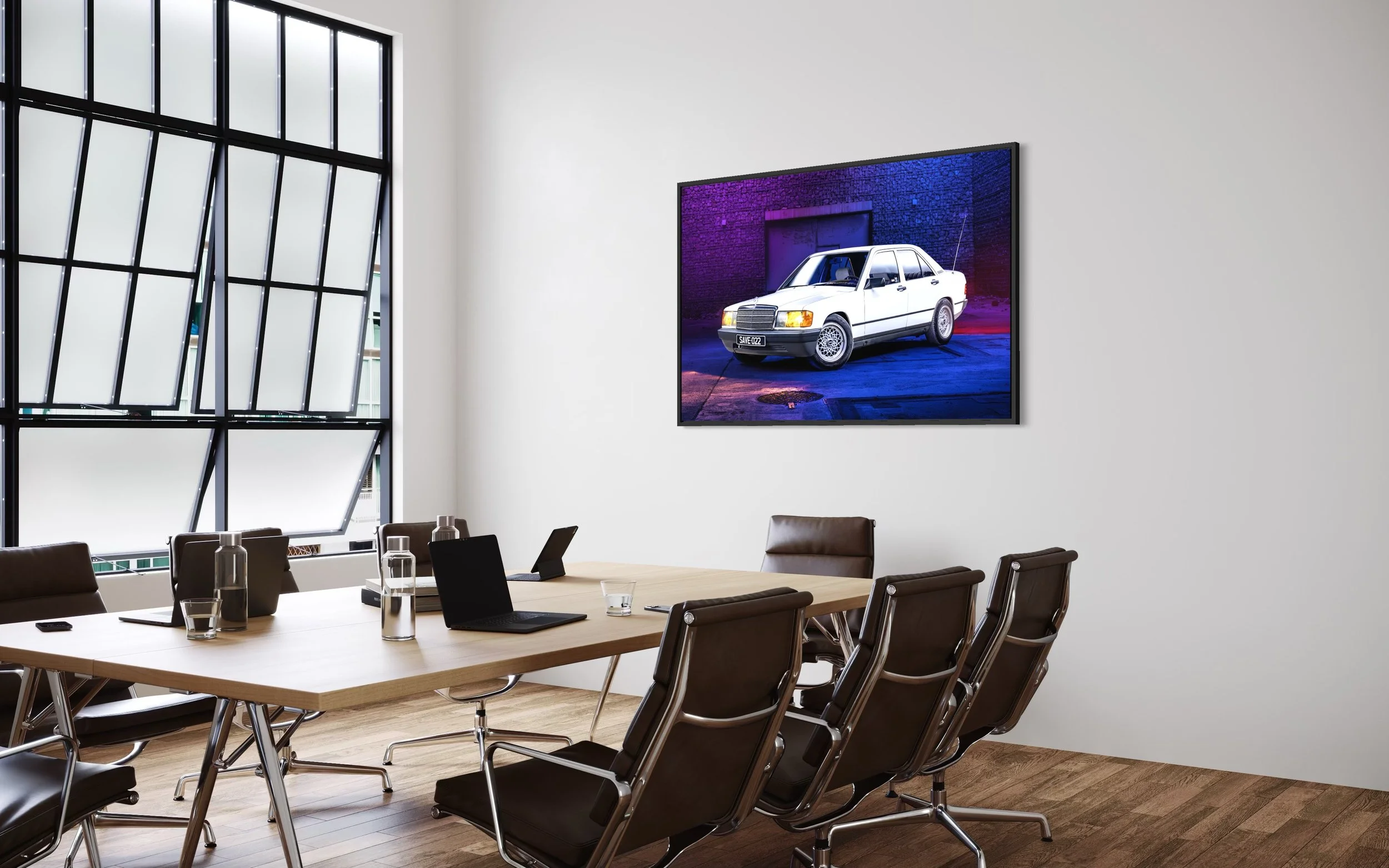 Salle de réunion moderne avec une grande table en bois, six chaises en cuir, deux ordinateurs portables, des bouteilles d'eau, des verres, et un écran mural affichant une voiture blanche dans un environnement urbain