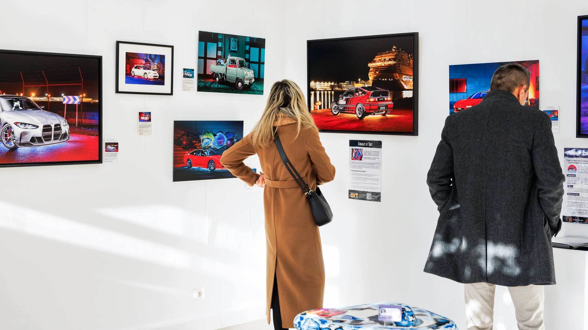 Deux personnes regardent des œuvres d'art représentant des voitures dans une galerie d'art