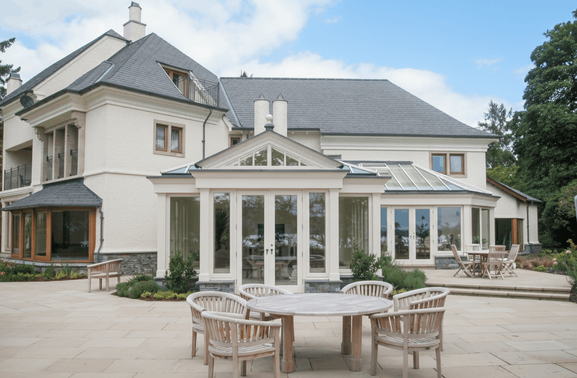 Large painted hardwood orangery with glazed roof lanterns and French doors extending across the rear of a substantial country home.