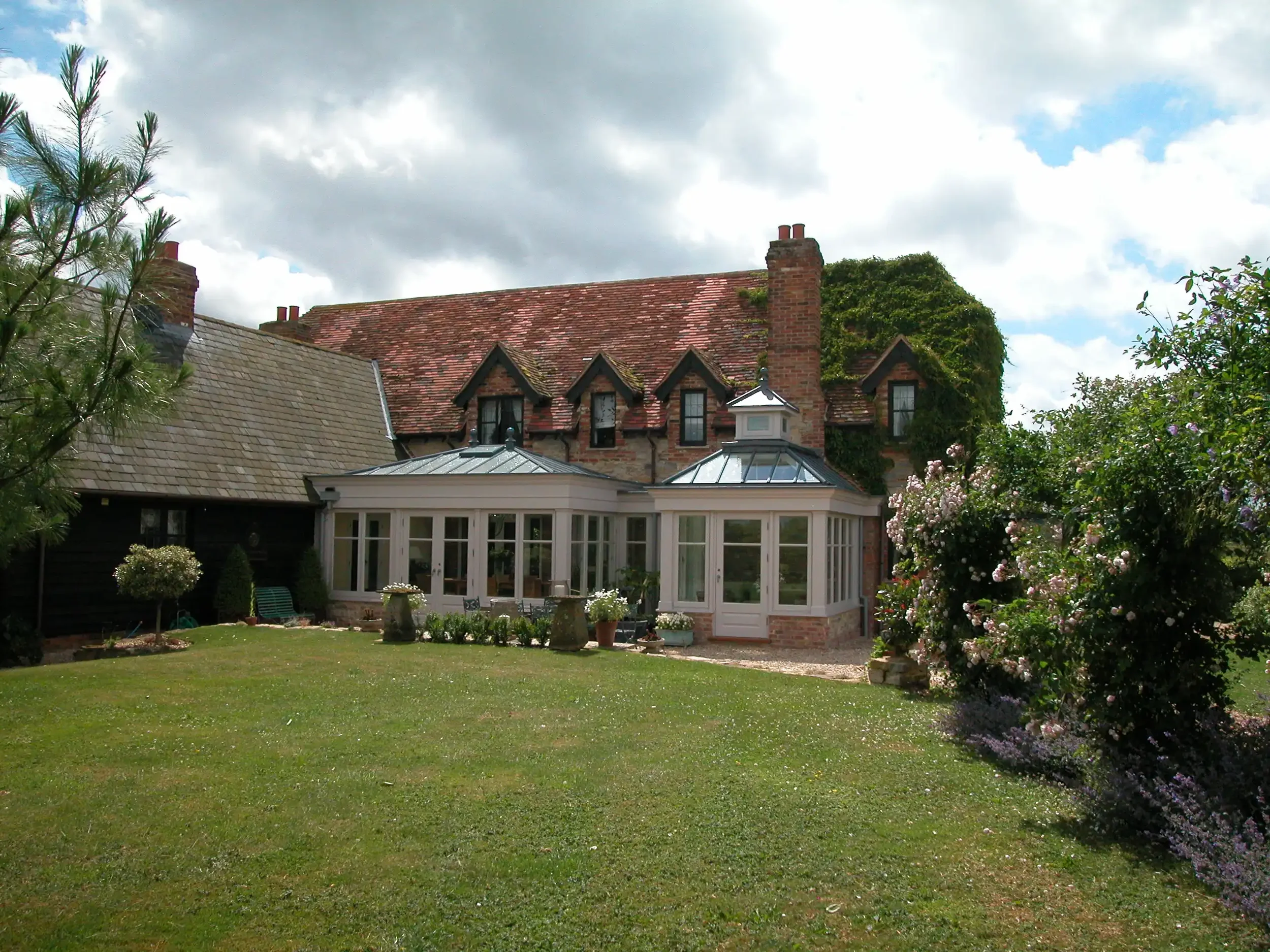 Wide exterior view of a large timber orangery extension attached to a period red brick property with a formal lawn.