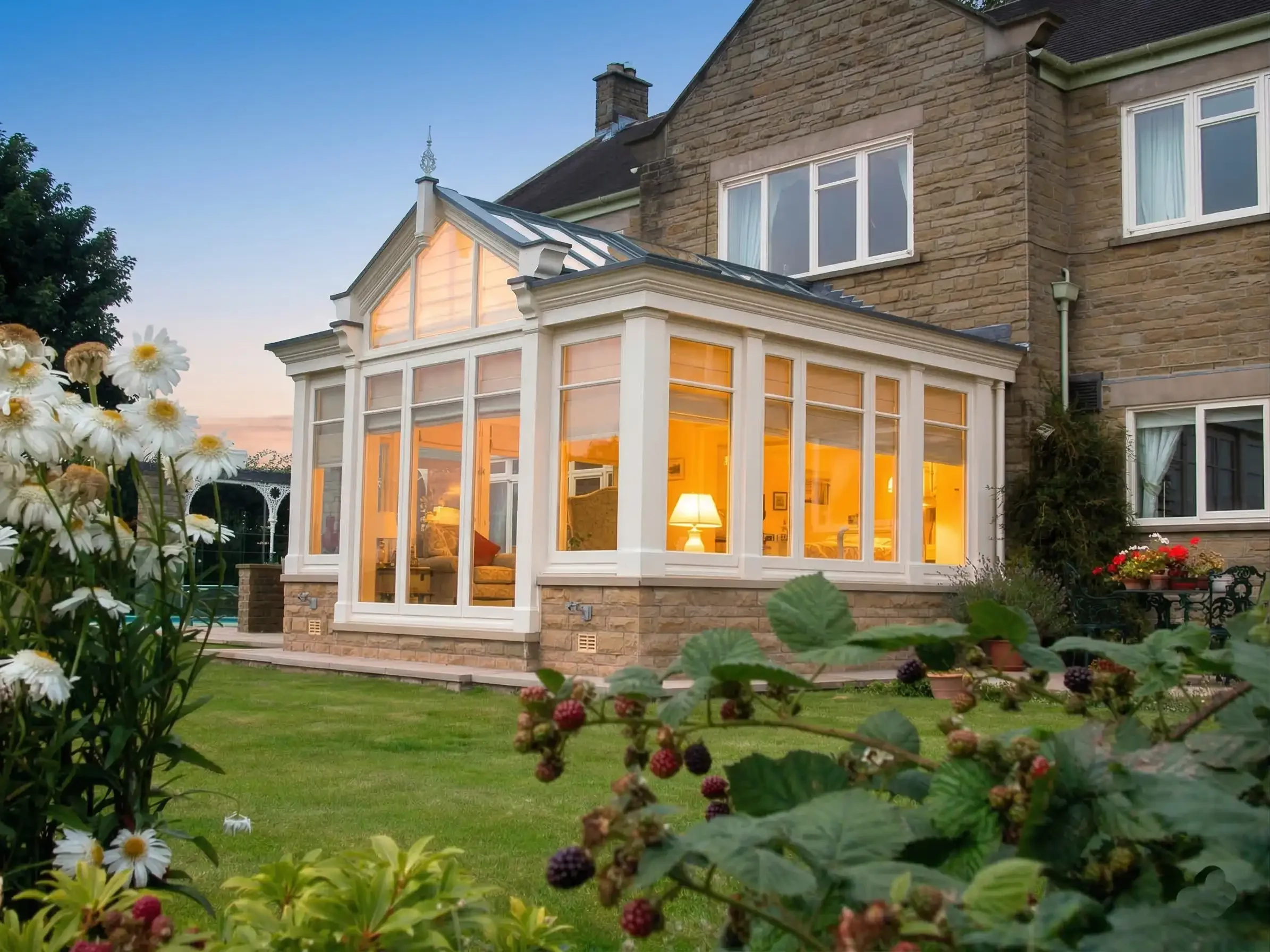 Exterior side view of a white timber extension on a stone house lit up from the inside at twilight.