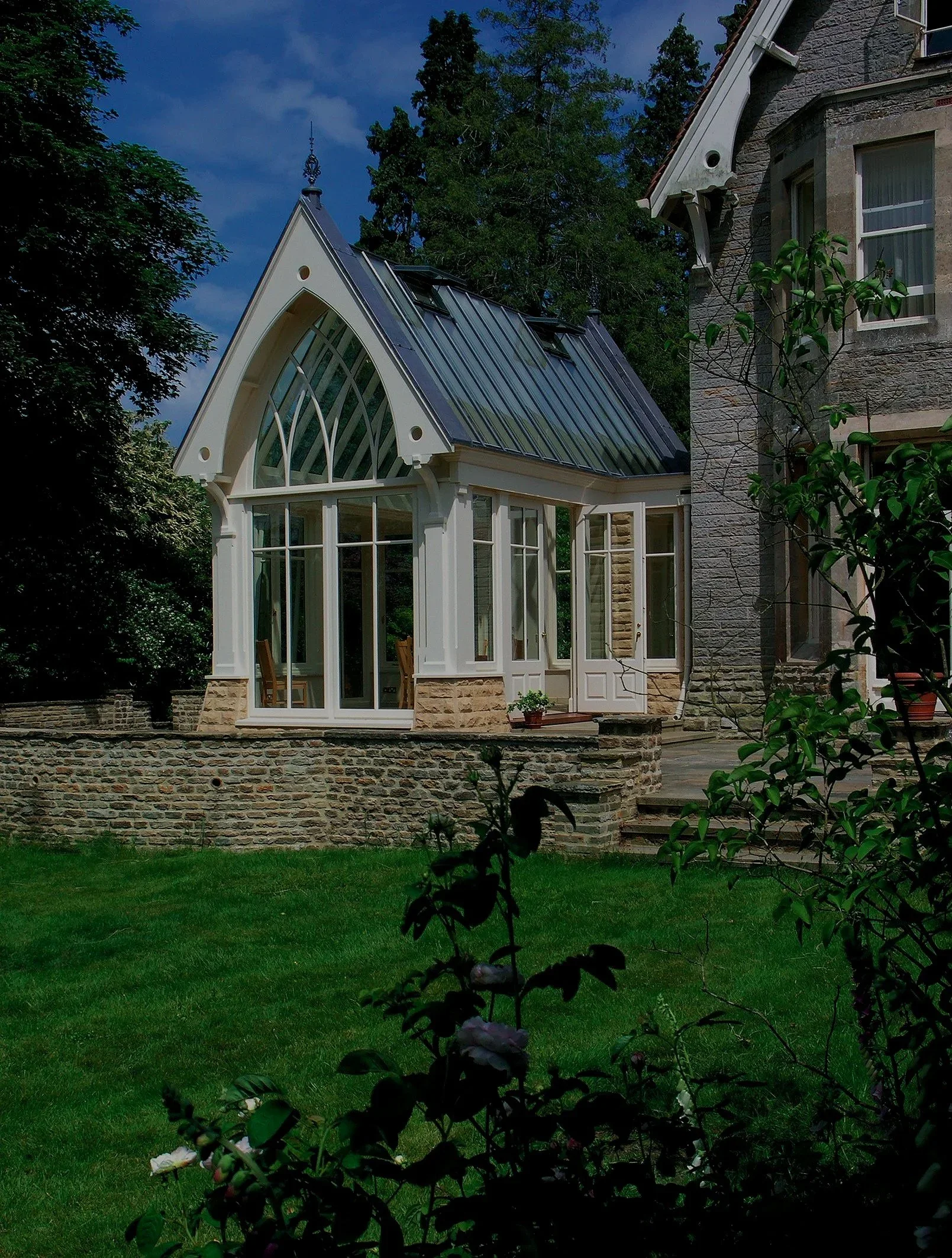 Bespoke white hardwood glazed extension with a steep Gothic-style roof attached to a period stone house.