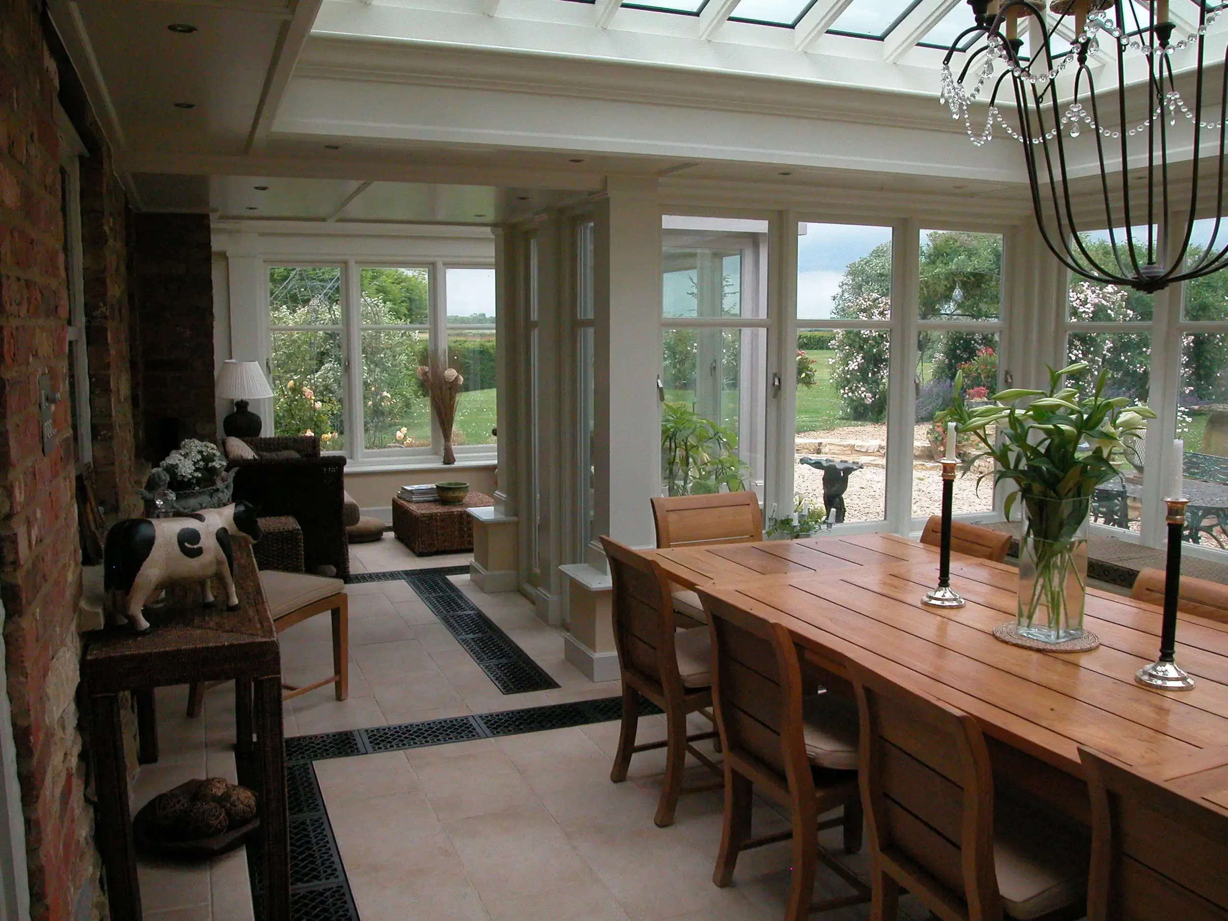 Interior of a large timber garden room extension showing an expansive farmhouse dining table set under a glass roof lantern.