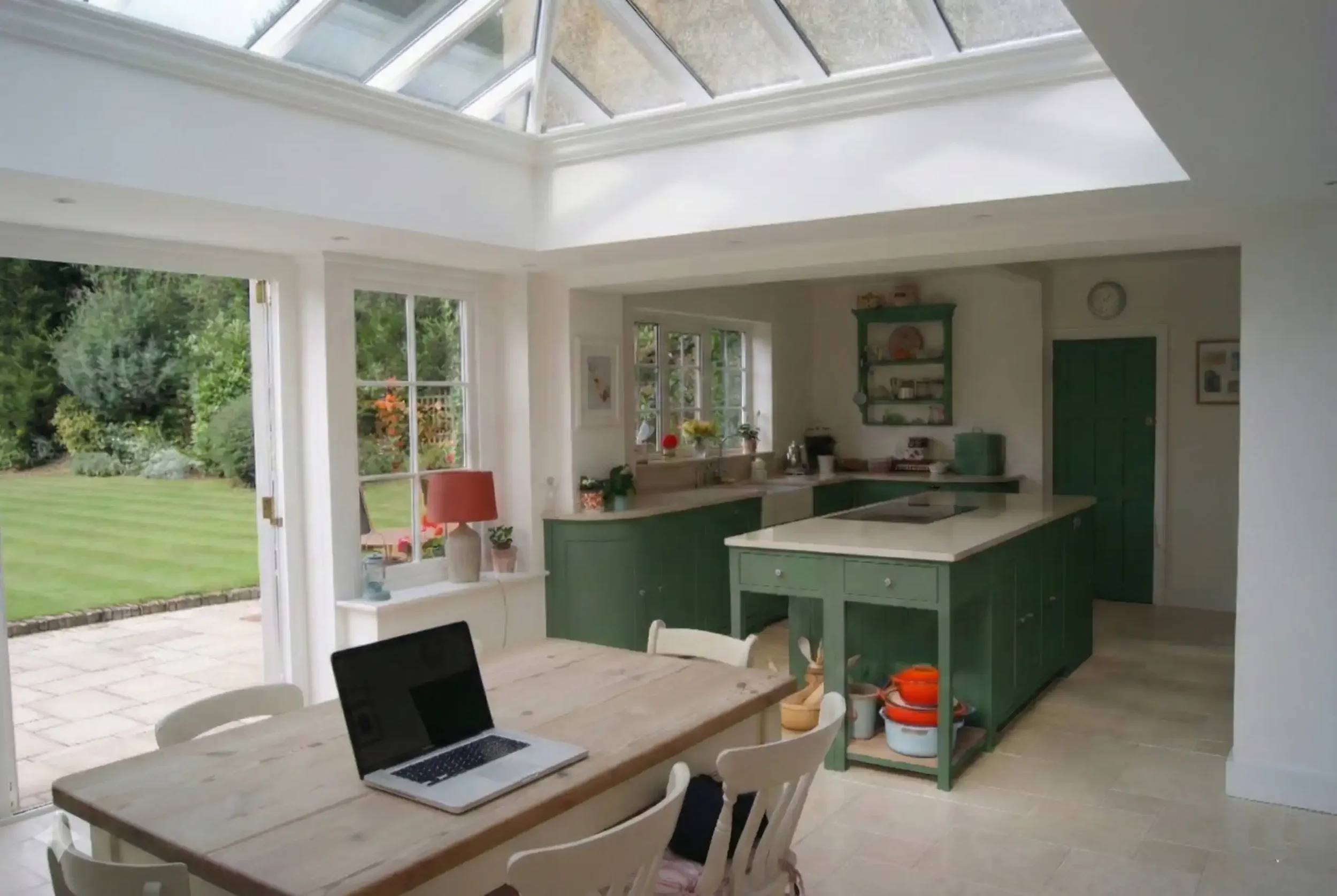 Open-plan kitchen and dining room with a large glazed roof lantern, garden-facing doors and green fitted kitchen.