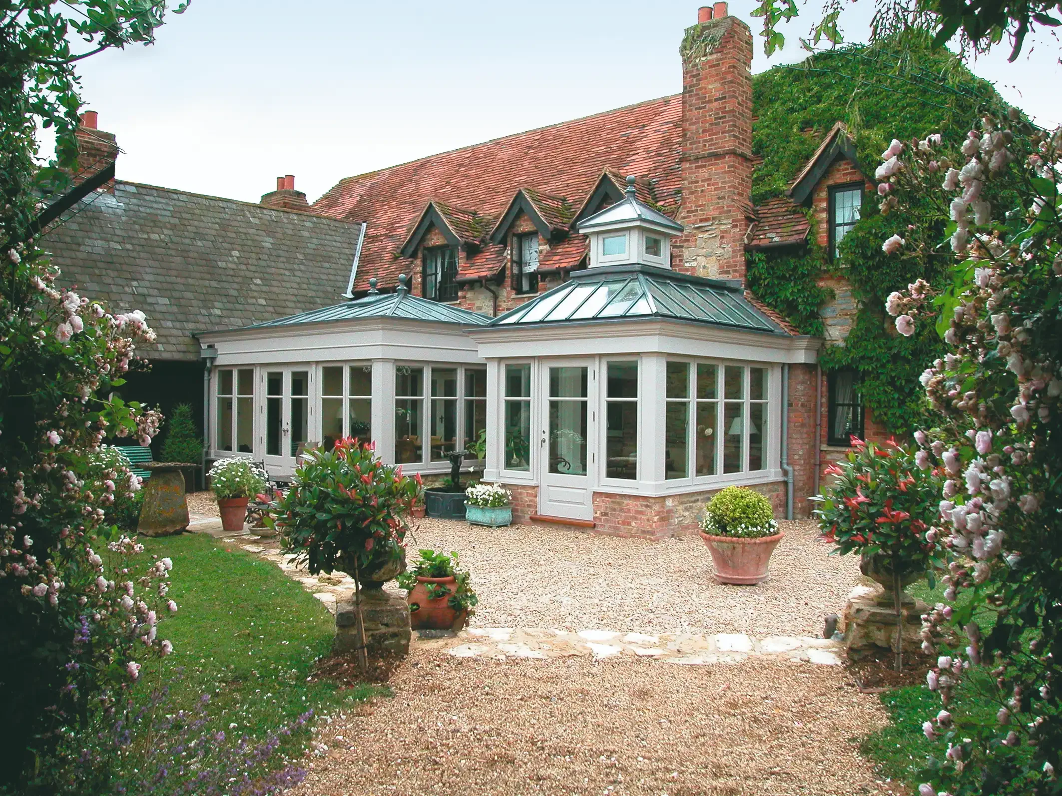 Traditional white hardwood orangery with roof lanterns extending from a period red-brick house surrounded by a mature garden
