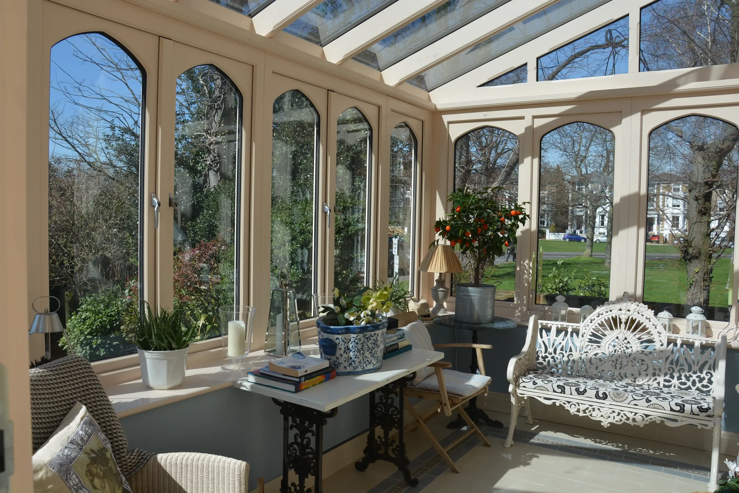Light-filled interior of a classic timber orangery showing decorative gothic arched window frames and views out to a mature garden.