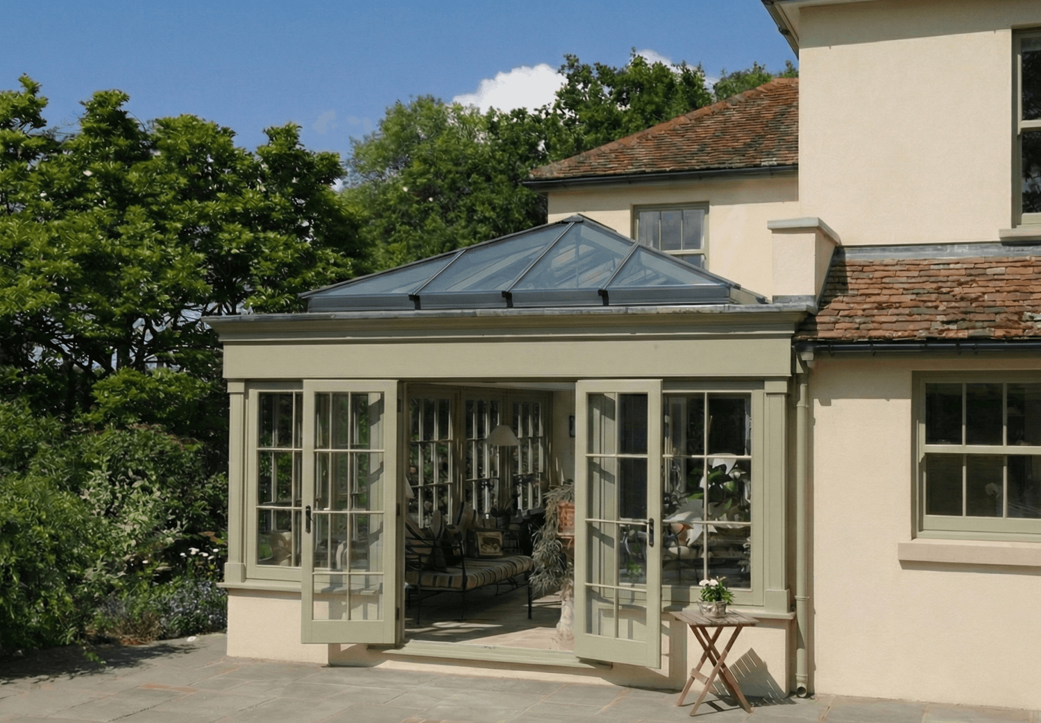 A grand hardwood orangery extension featuring a glazed roof lantern and traditional stone pillars in the Cotswolds.