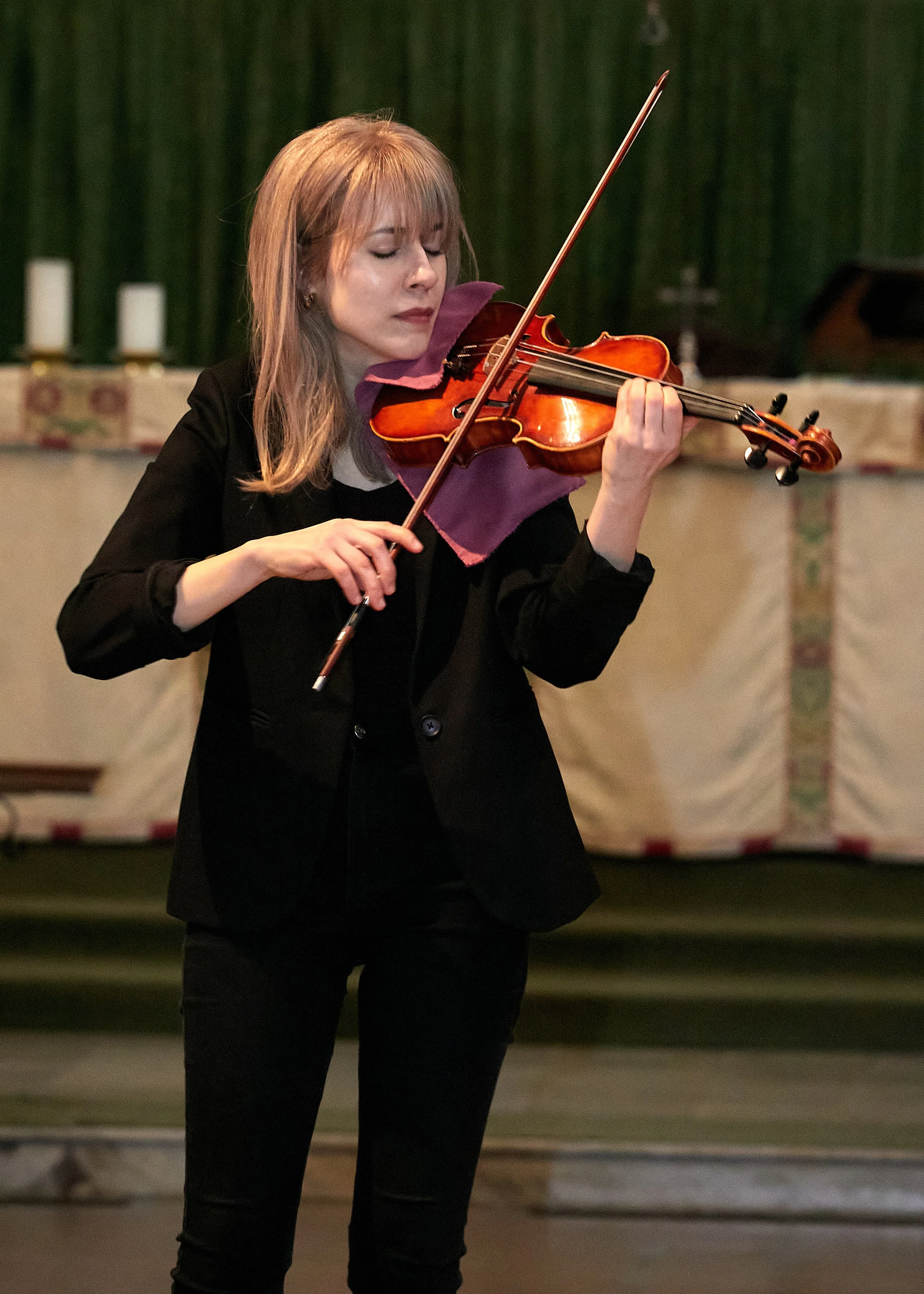 Talia Ramos standing and performing a solo violin piece in a church for a wedding